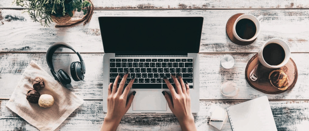 image of hands typing on a laptop with headphone, coffee and donuts